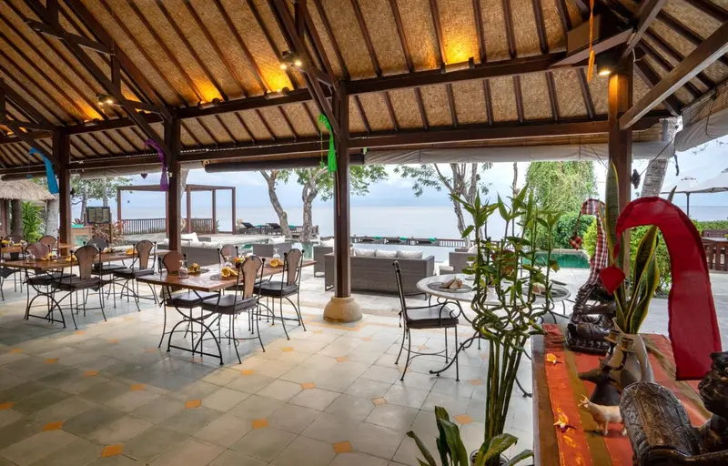 Une salle à manger extérieure avec des tables et des chaises, donnant sur une vue sur la mer.