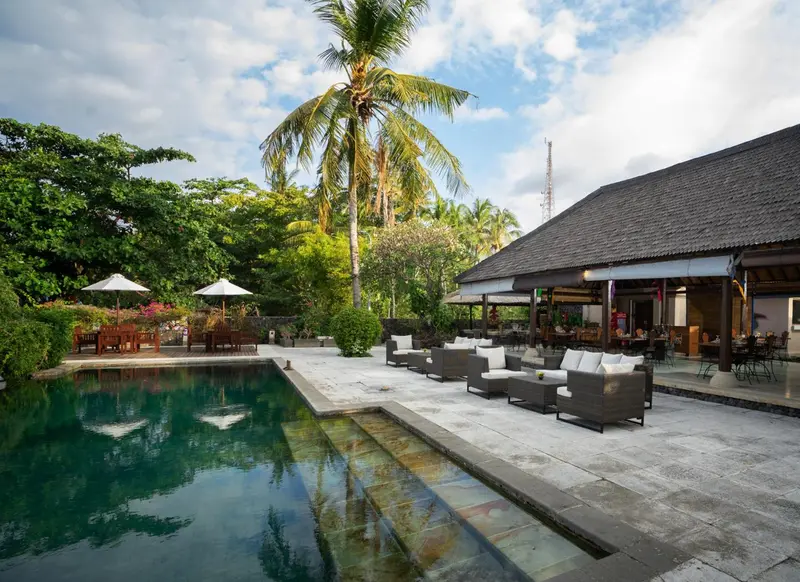 Une piscine bordée d'une terrasse avec des salons de jardin et un bâtiment à toit sombre.