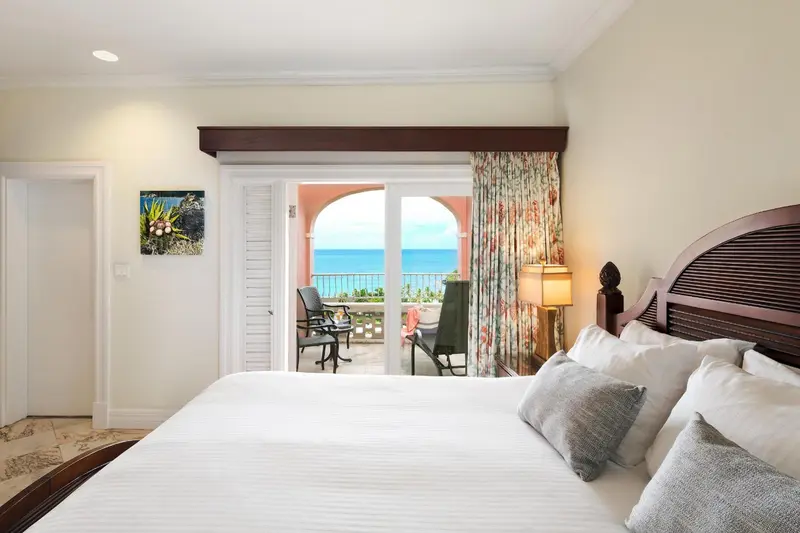 Une chambre lumineuse avec un grand lit donnant sur une terrasse et la mer.