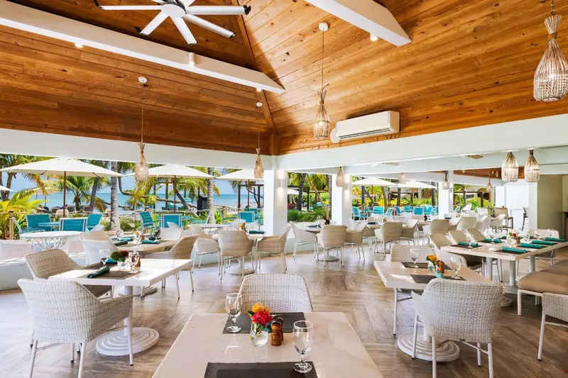 Une salle à manger lumineuse avec des tables dressées et vue sur la mer.