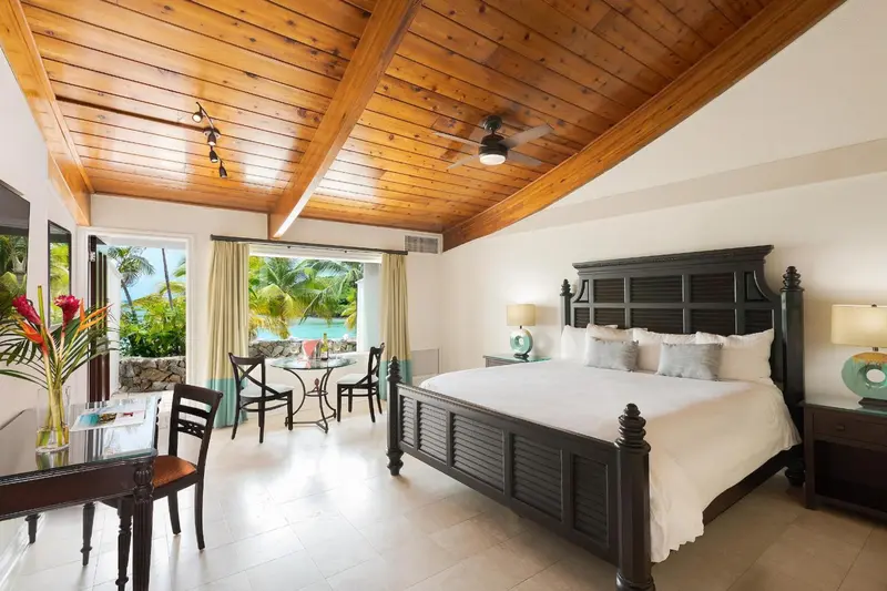 Une chambre lumineuse avec un grand lit et un coin repas près d'une baie vitrée.