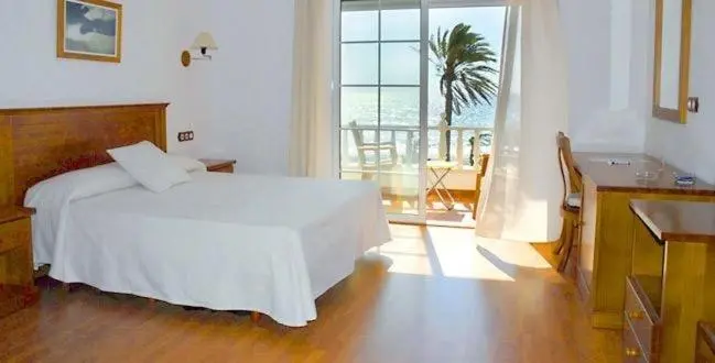 Une chambre lumineuse avec un lit fait et une vue sur la mer depuis un balcon.