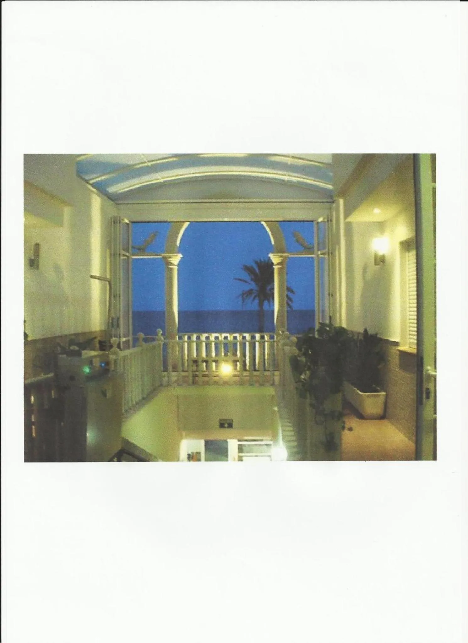 Vue d'une terrasse avec une rambarde blanche et des colonnes ouvrant sur la mer au crépuscule.