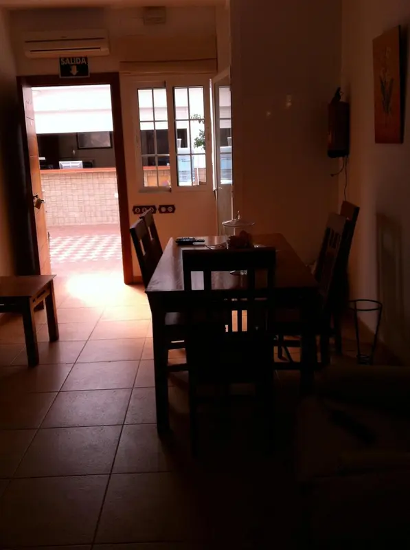 Une table en bois et des chaises se trouvent dans une pièce lumineuse avec une porte ouverte sur un espace extérieur.