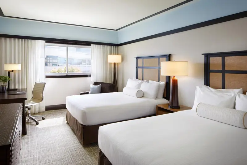 Une chambre d'hôtel lumineuse avec deux lits et un bureau.