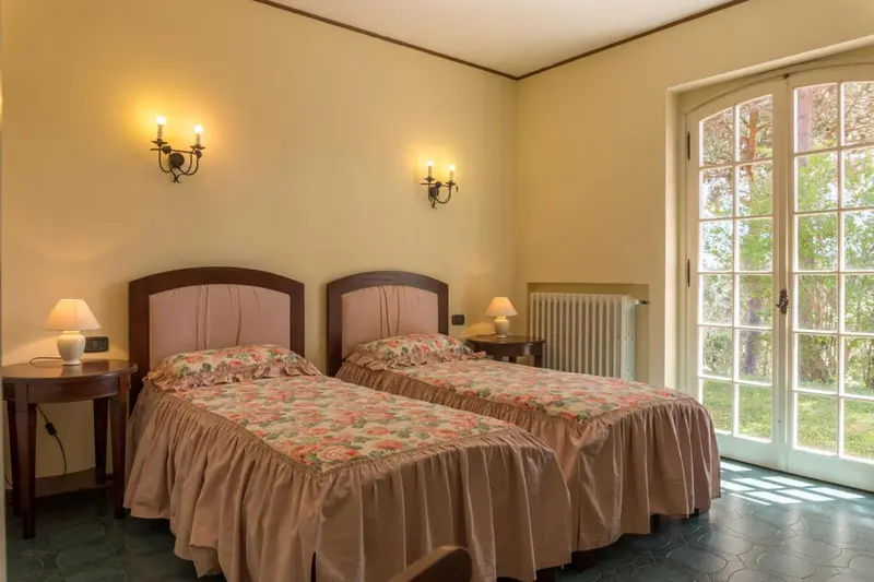 Chambre lumineuse avec deux lits simples et une porte-fenêtre donnant sur un jardin.