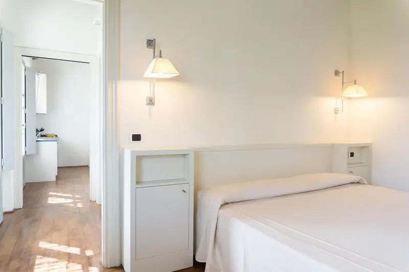 Une chambre lumineuse avec un lit simple et un accès à une cuisine.