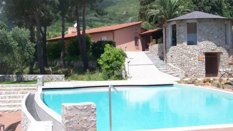 Une piscine au premier plan, avec un bâtiment en pierre et des escaliers menant à une terrasse.