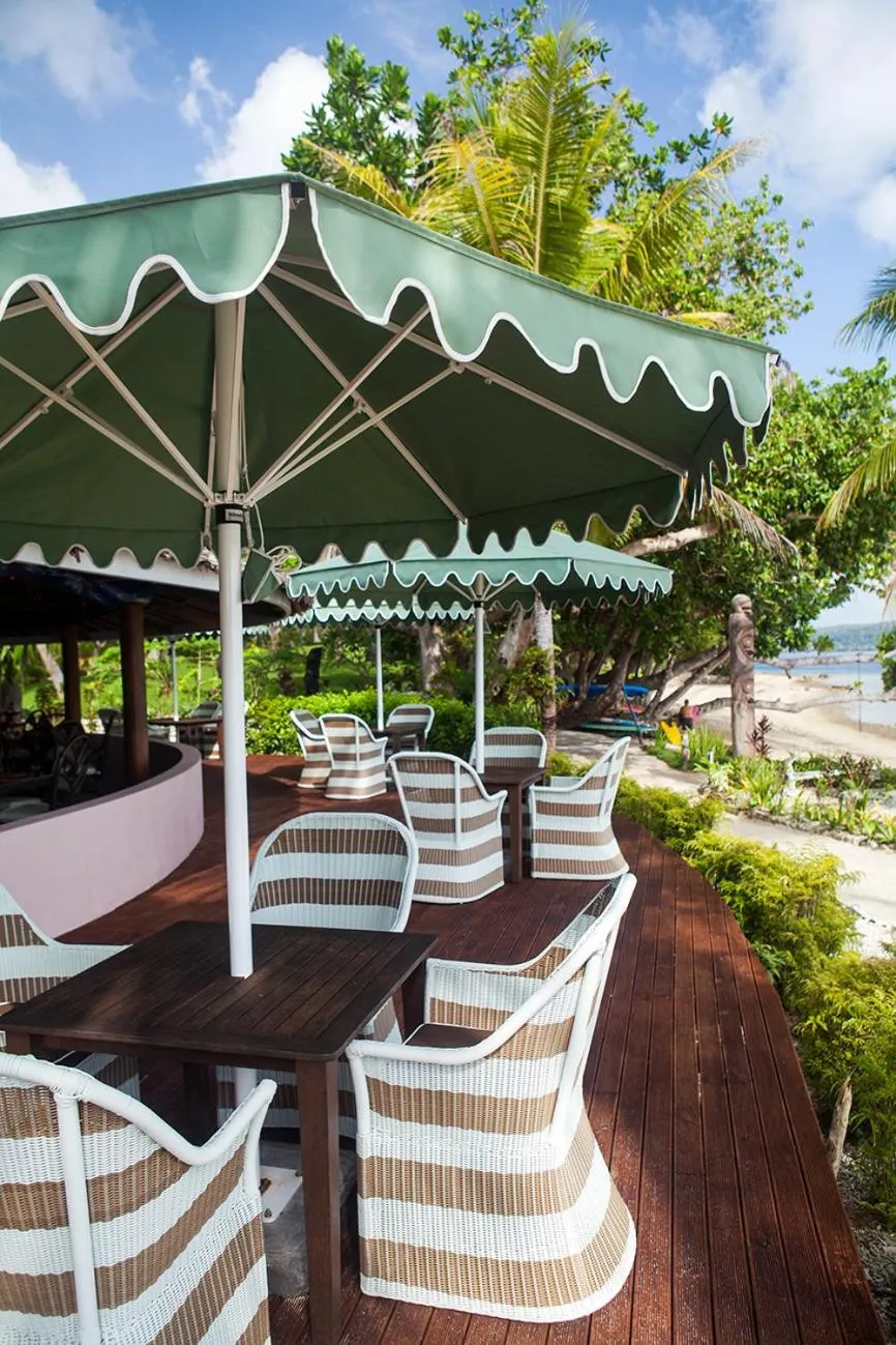 Terrasse ombragée avec mobilier de jardin en osier et vue sur la mer.