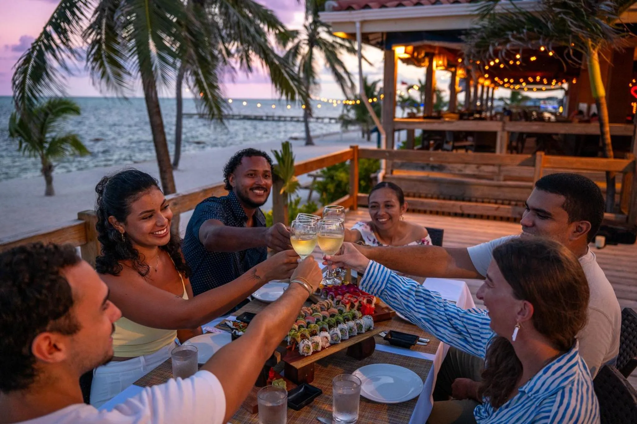 Un groupe de personnes trinque avec des verres sur une terrasse en bord de mer.