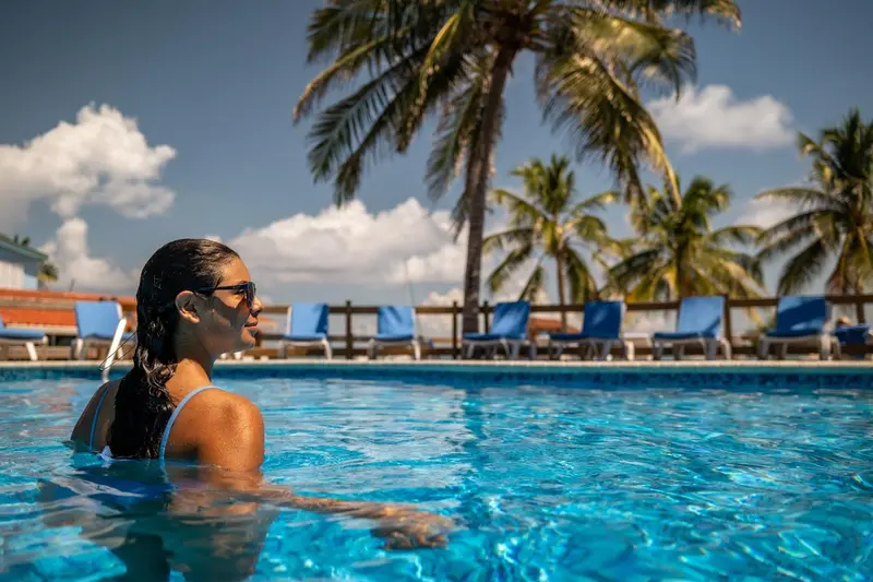 Une femme se tient dans une piscine, regardant vers des palmiers.