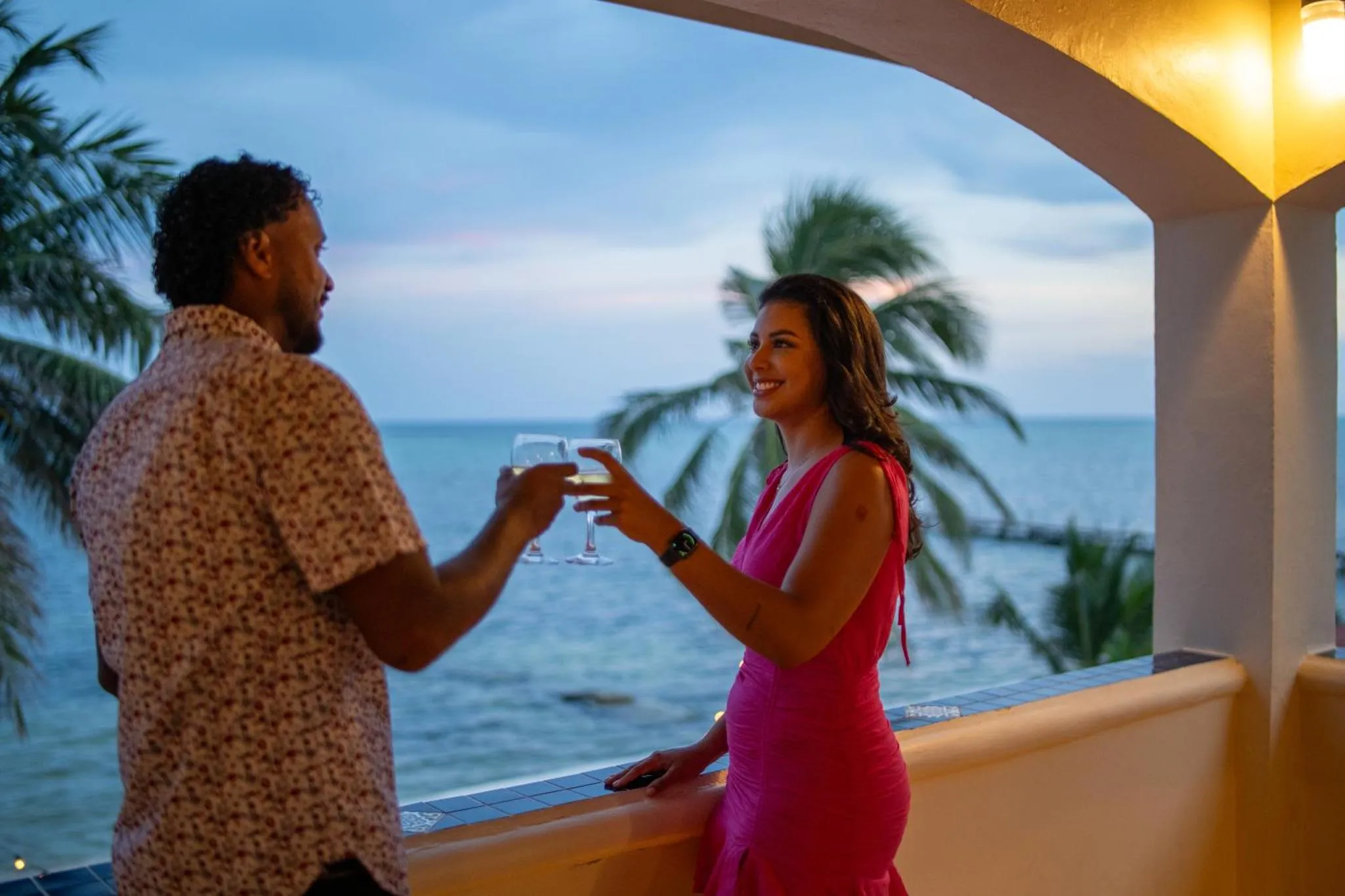 Un couple trinque sur une terrasse avec vue sur la mer au crépuscule.