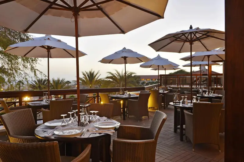 Tables dressées sur une terrasse ombragée avec vue sur la mer.