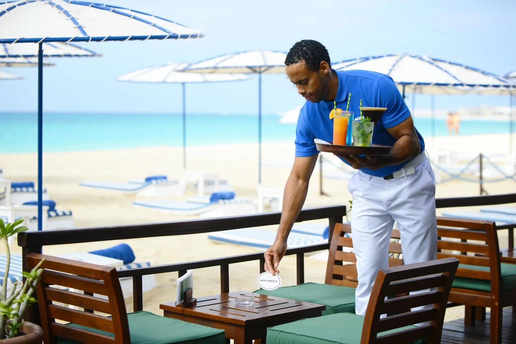 Un serveur apporte des boissons à une table en terrasse face à la mer.