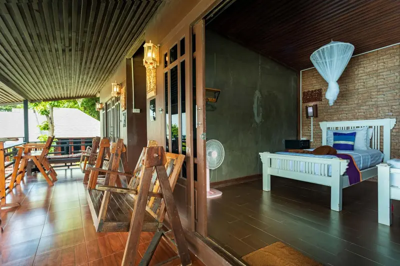 Une chambre lumineuse s'ouvre sur une terrasse couverte avec des fauteuils en bois.