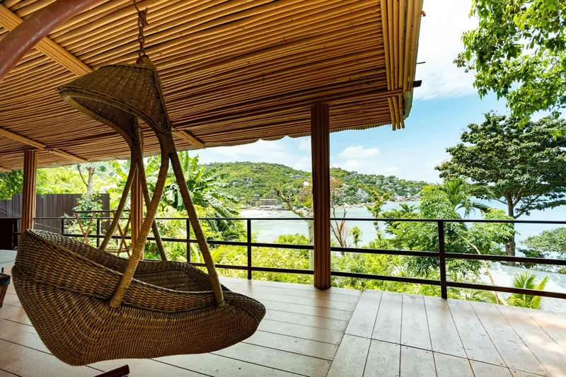 Un hamac suspendu sous une structure en bambou offre une vue sur la mer et la végétation.