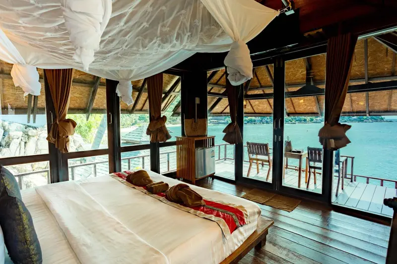Une chambre avec un grand lit à baldaquin donnant sur une terrasse et la mer.
