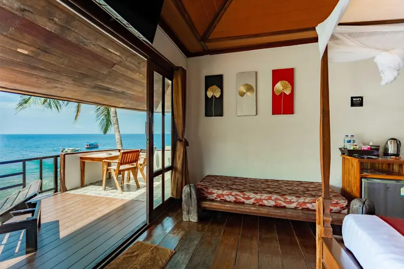 Une chambre lumineuse s'ouvre sur une terrasse en bois avec vue sur la mer.