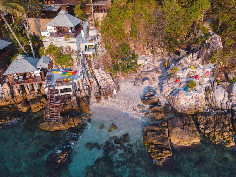 Vue aérienne d'une plage rocheuse avec des bungalows et des transats colorés.
