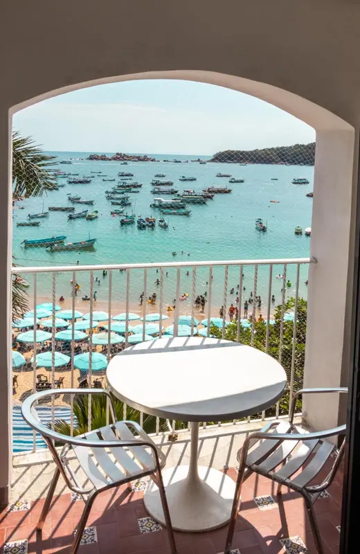 Une table et des chaises blanches se trouvent sur une terrasse carrelée avec vue sur une plage et la mer.