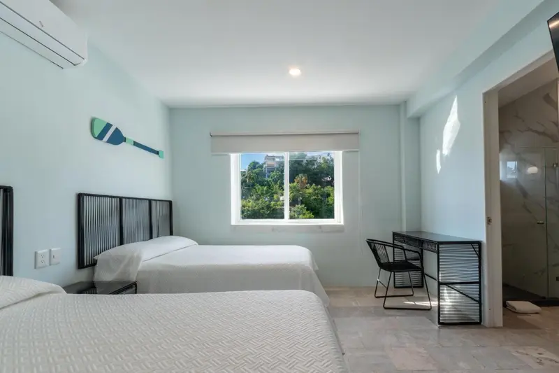 Une chambre lumineuse avec deux lits simples et un bureau près d'une fenêtre.