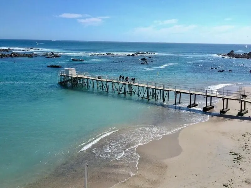 Un ponton en bois s'avance sur une mer turquoise et une plage de sable.