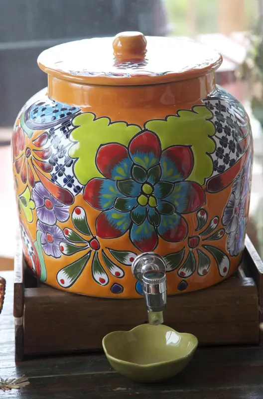 Une jarre en céramique colorée avec un robinet et un verre.