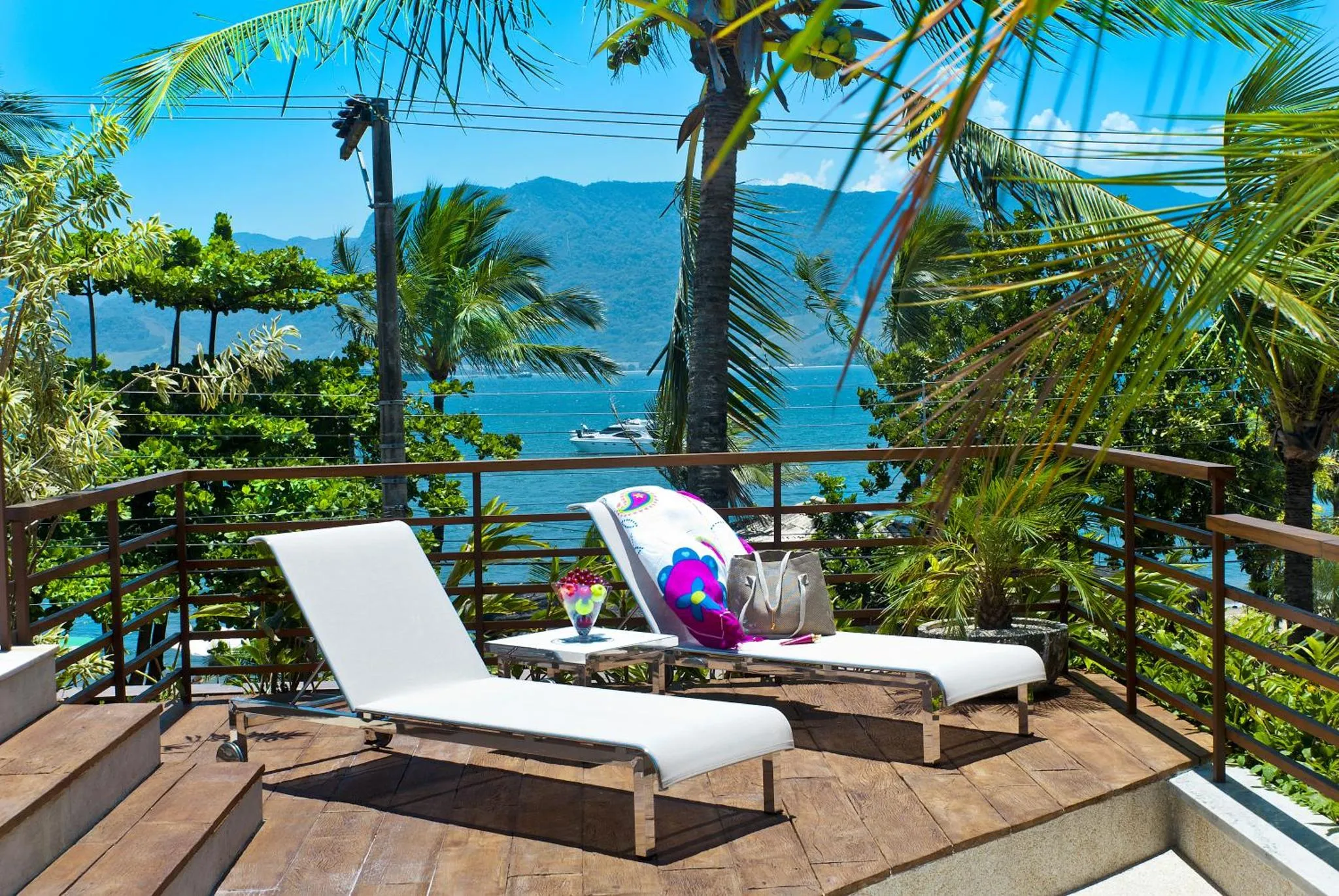 Deux transats blancs sur une terrasse en bois avec vue sur la mer et les montagnes.