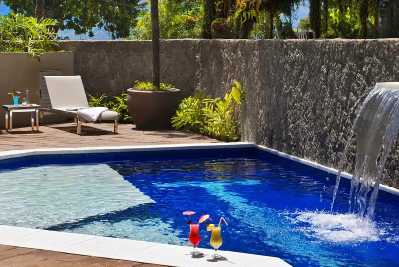 Une piscine avec une cascade et des boissons colorées sur le bord.