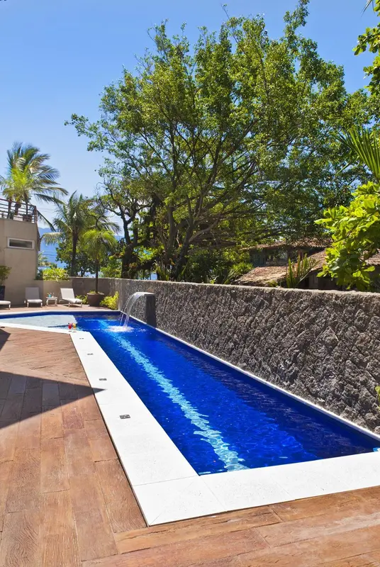 Une piscine rectangulaire bordée d'une terrasse en bois et d'un mur en pierre.