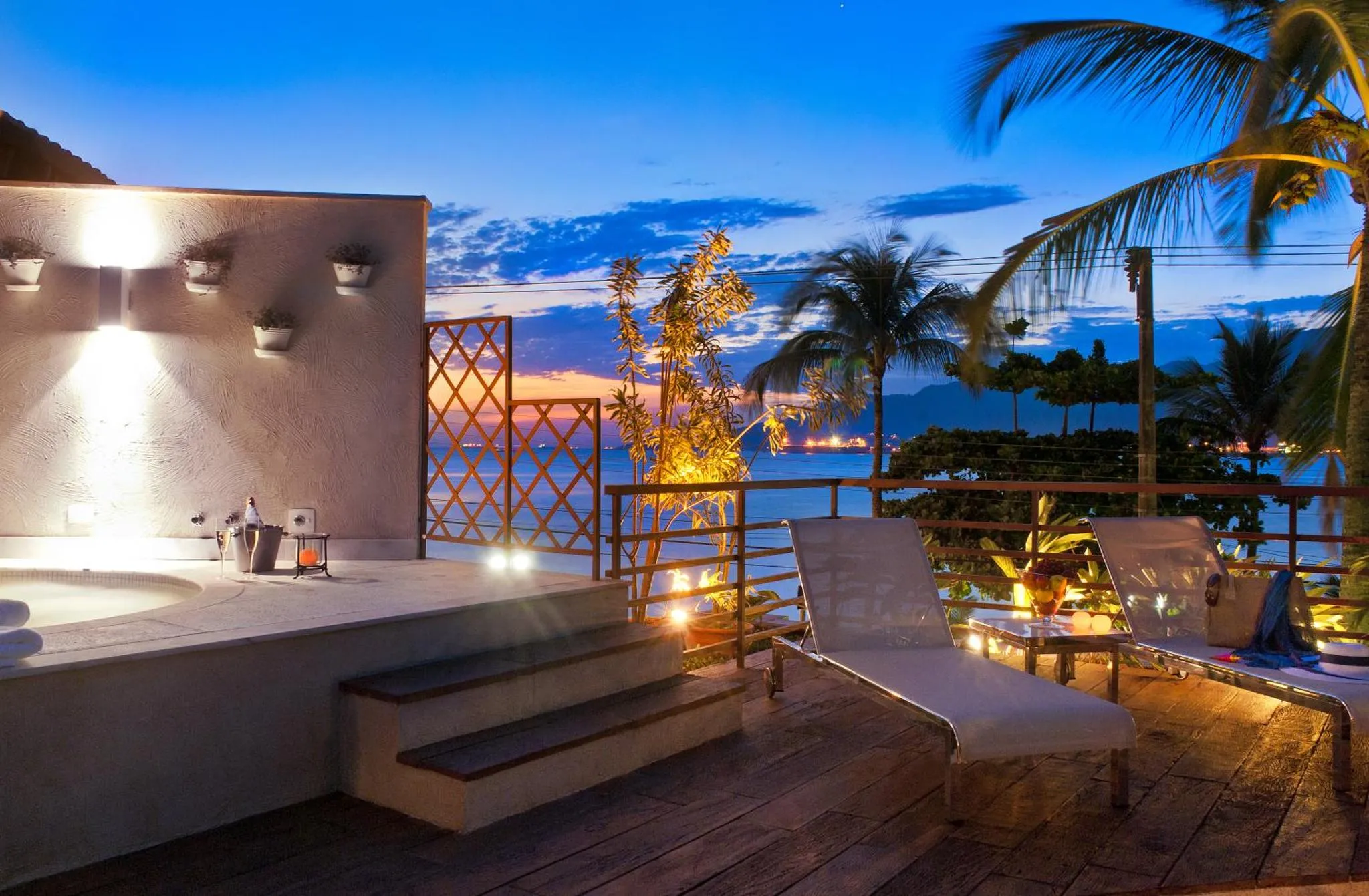 Terrasse avec jacuzzi et mobilier de relaxation face à la mer au crépuscule.