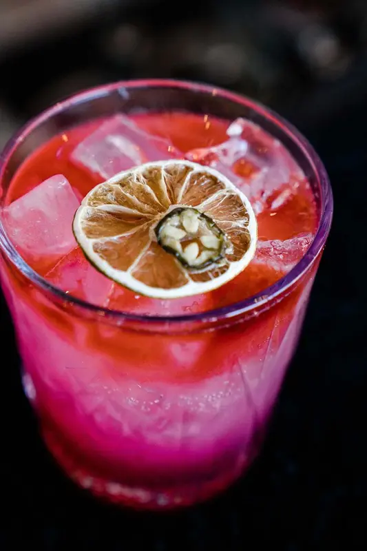 Un cocktail rose vif avec une rondelle de citron déshydratée.