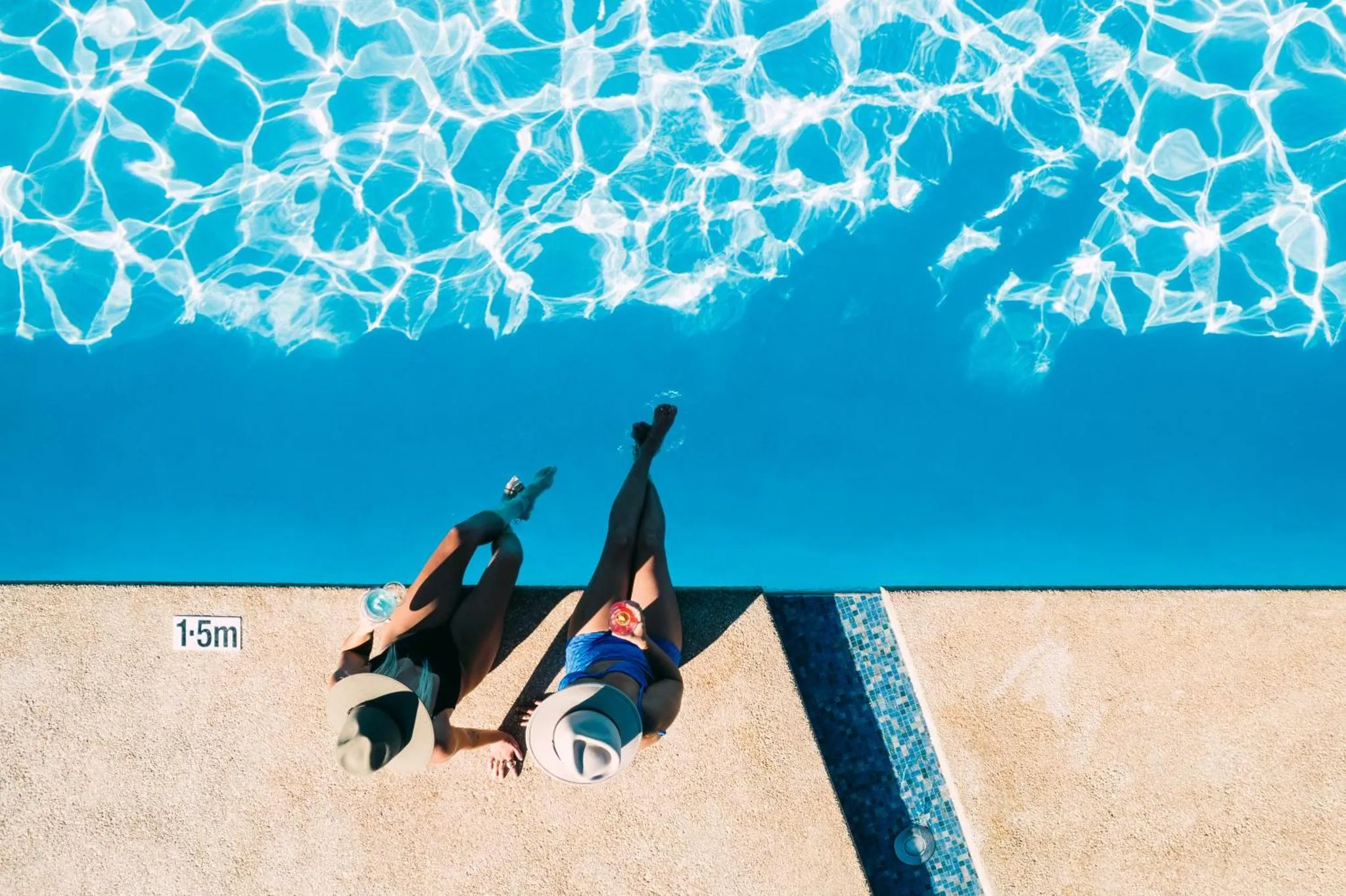 Deux personnes se détendent au bord d'une piscine bleu vif.