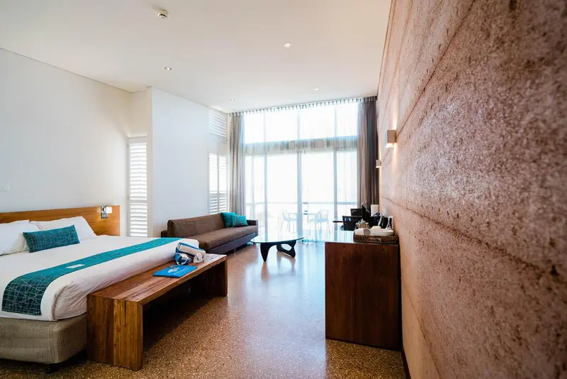 Une chambre lumineuse avec un grand lit et un canapé face à une baie vitrée.