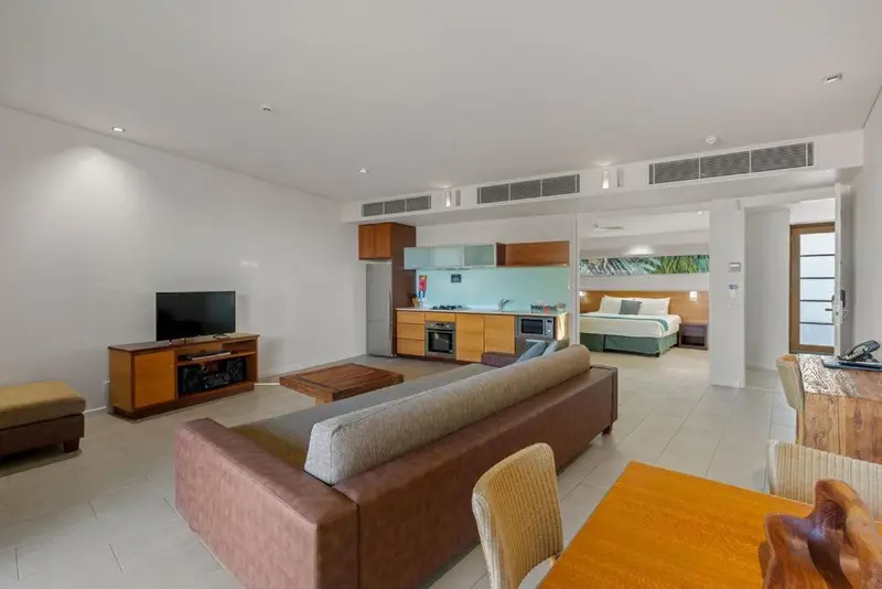 Espace de vie lumineux avec canapé, télévision et cuisine ouverte sur une chambre.