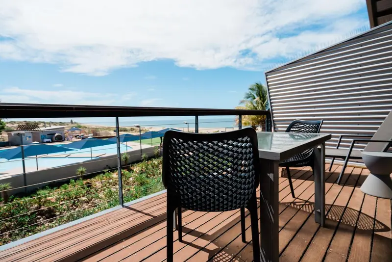 Terrasse avec mobilier en plastique noir donnant sur une plage et une piscine.
