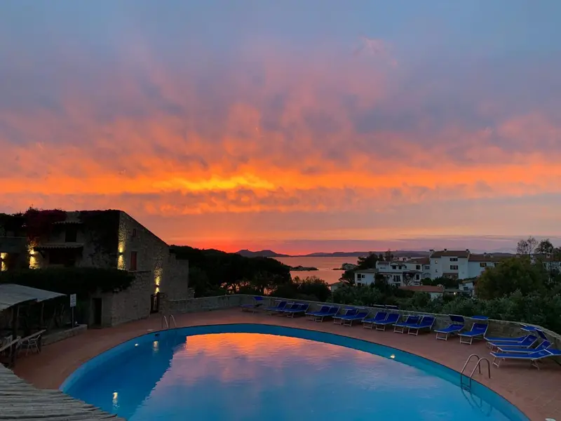 Une piscine illuminée reflète les couleurs d'un coucher de soleil sur la mer.