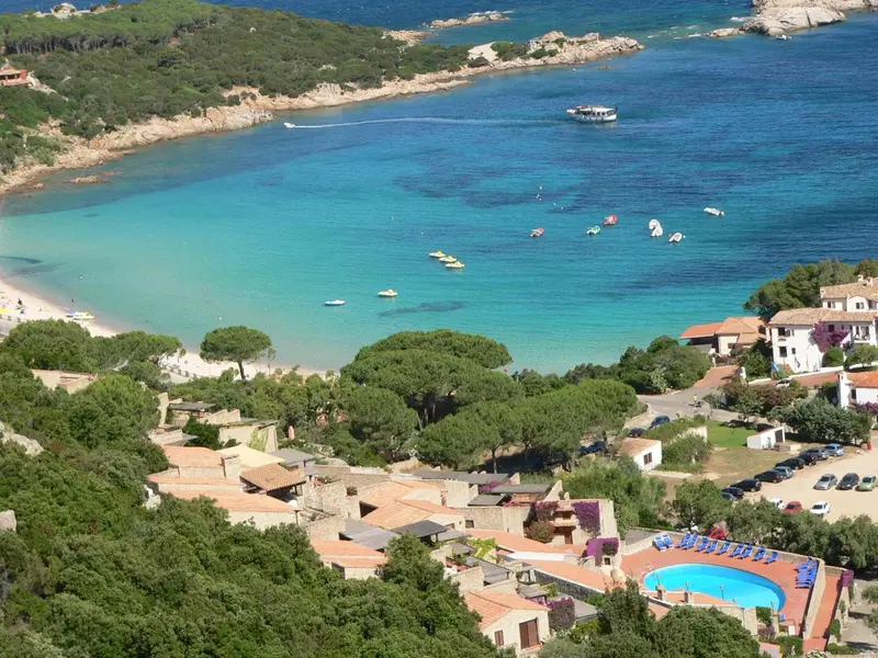 Vue aérienne d'une crique turquoise bordée de pins et d'un complexe hôtelier.