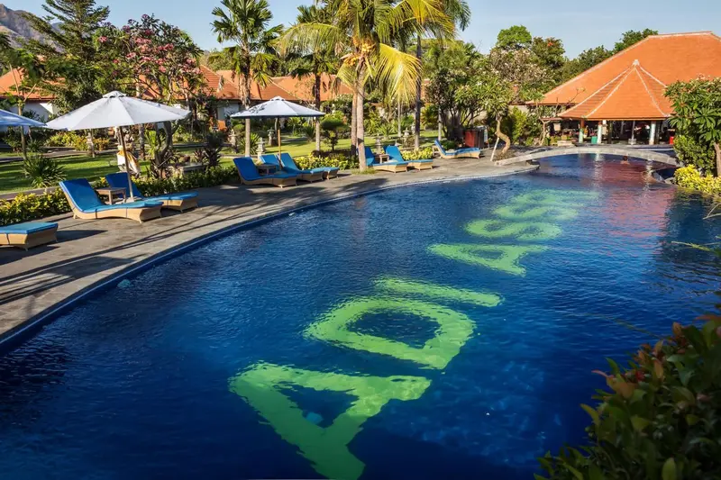 Transats bleus alignés au bord d'une piscine turquoise dans un jardin tropical.
