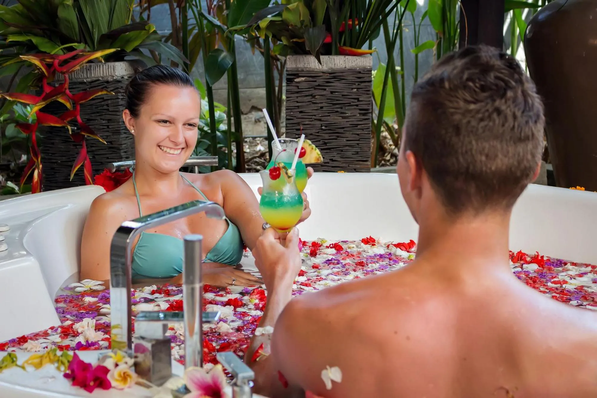 Un couple se détend dans un bain à remous fleuri avec des boissons colorées.