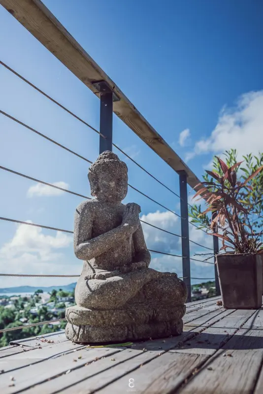 Statue de Bouddha sur une terrasse en bois avec vue sur la mer et la végétation.