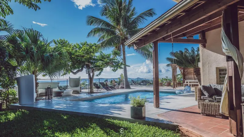 Une piscine bordée de chaises longues offre une vue sur la mer et la végétation tropicale.