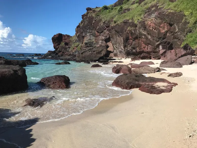 Une plage de sable fin bordée d'eau turquoise et de rochers volcaniques.