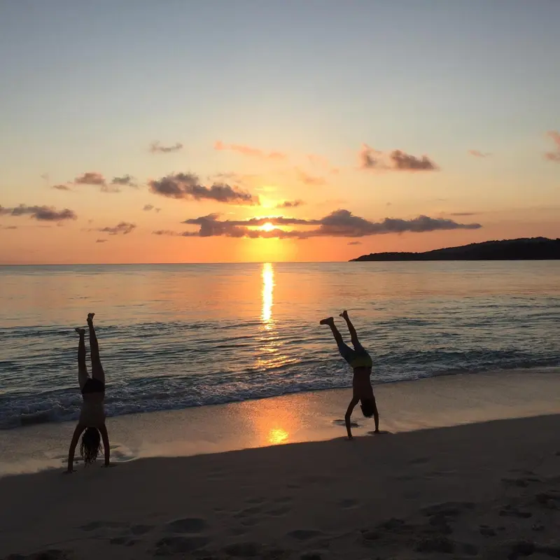 Deux silhouettes font des roulades sur une plage au coucher du soleil.