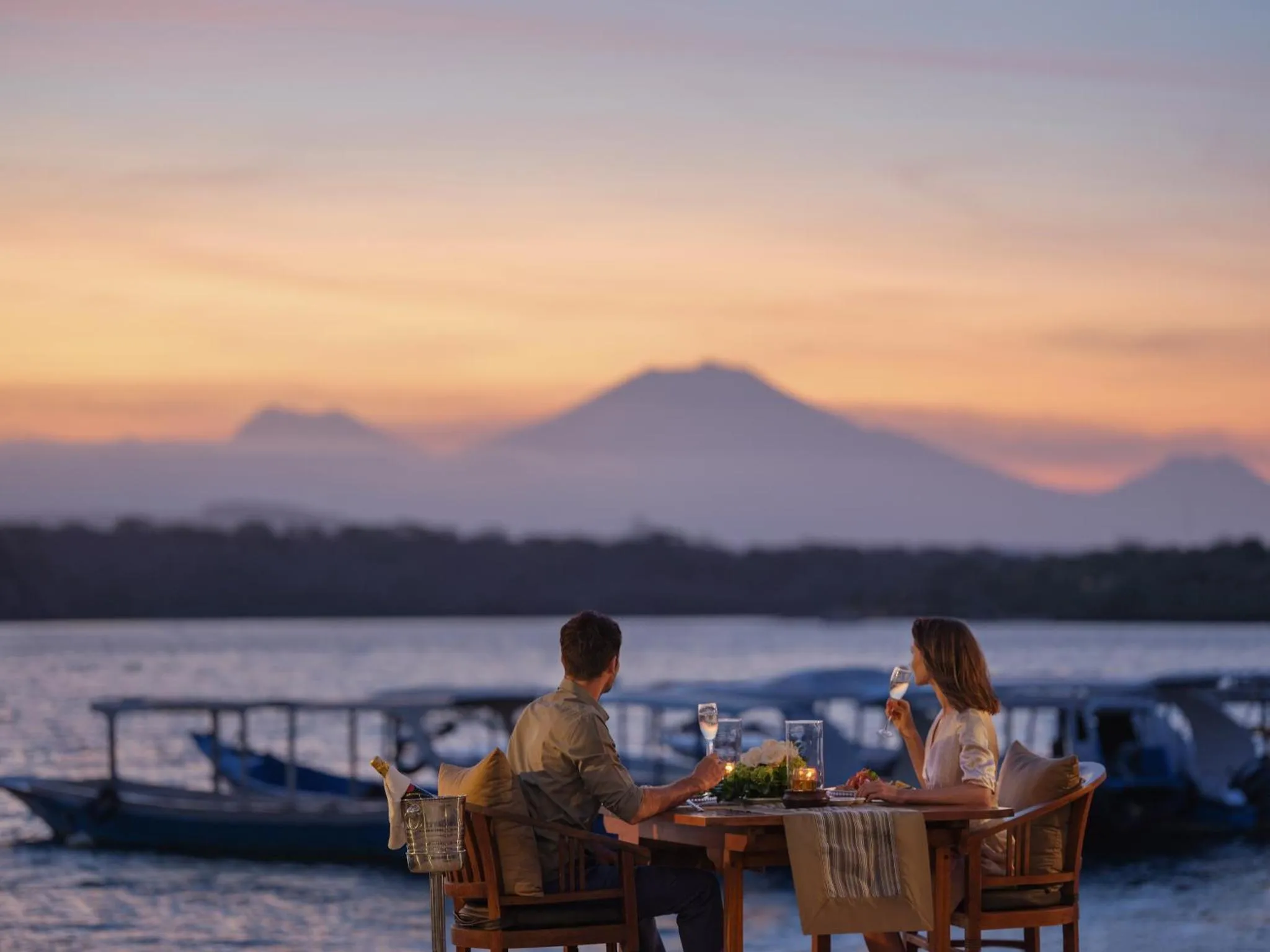 Un couple déguste des boissons sur une terrasse face à la mer au coucher du soleil.