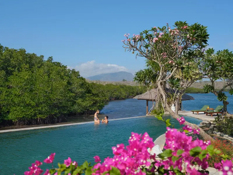 Deux personnes se détendent dans une piscine bordée de végétation tropicale.