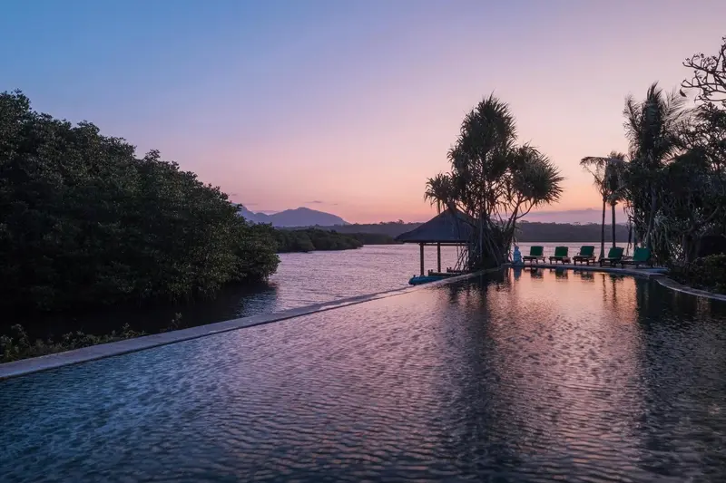 Une piscine à débordement surplombe une rivière au coucher du soleil.