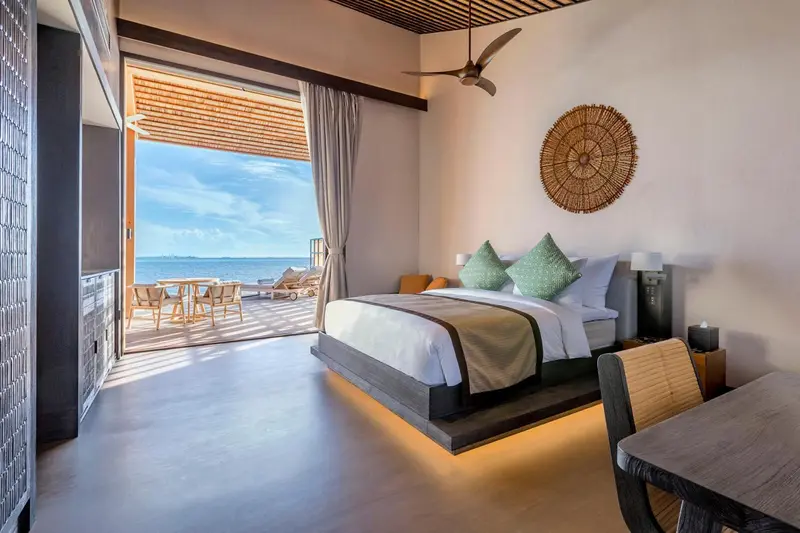 Chambre lumineuse avec un grand lit et une vue sur la mer depuis une terrasse.