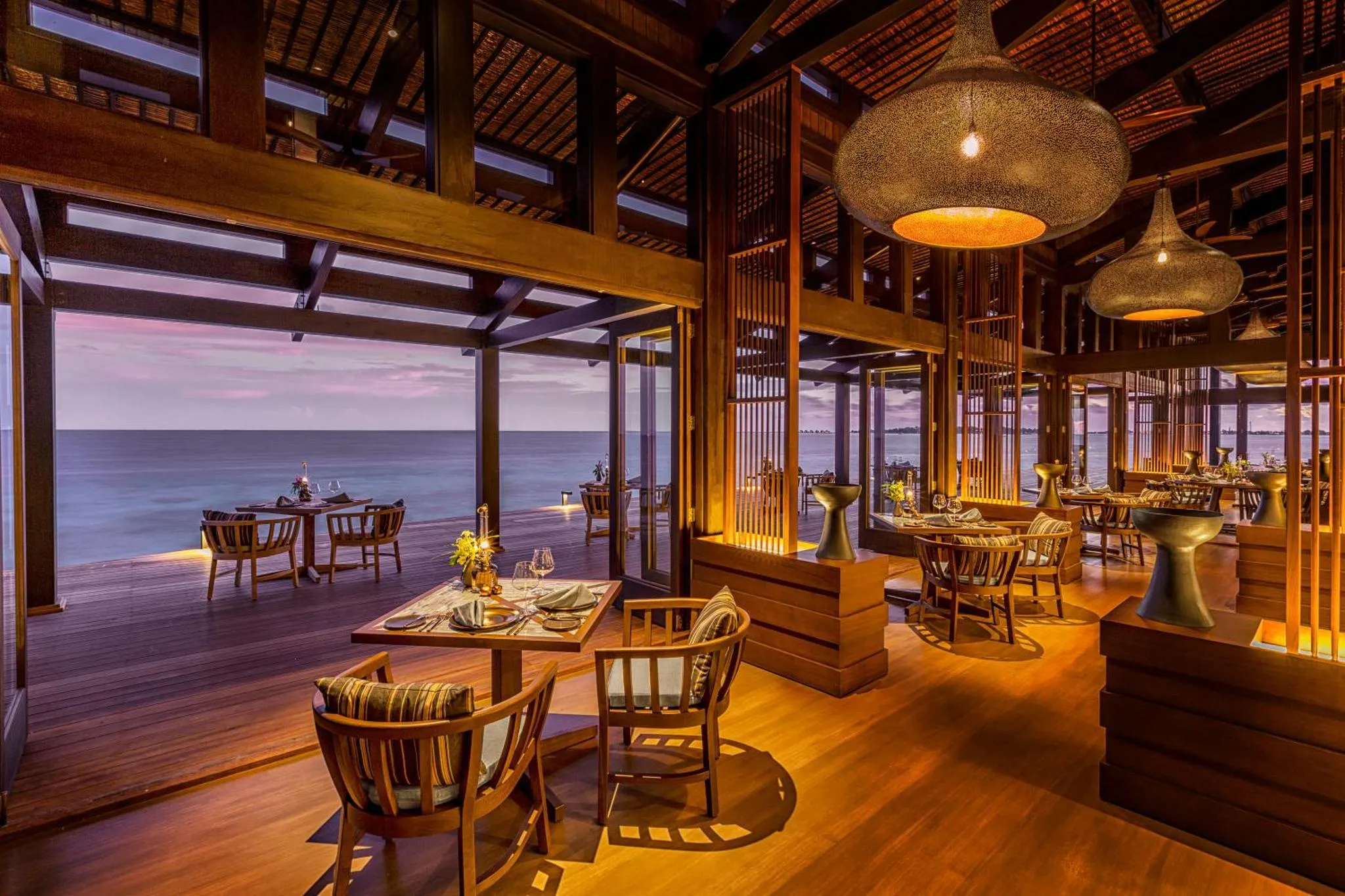Une salle à manger ouverte sur une vue de mer au coucher du soleil.