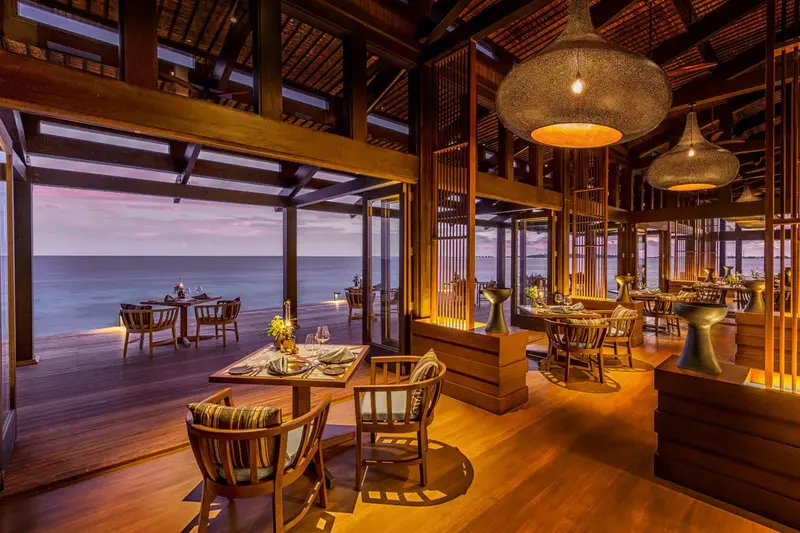 Une salle à manger ouverte sur une vue de mer au coucher du soleil.